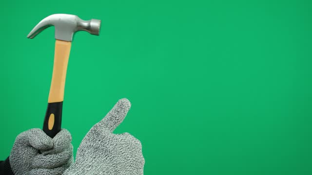 A man's hand in gray gloves holds a hammer on a green background