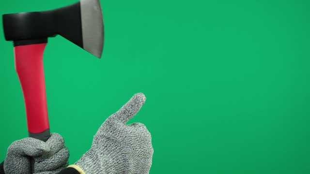 A man's hand holds an ax on a green background wearing gray gloves. Thumbs up shows good class
