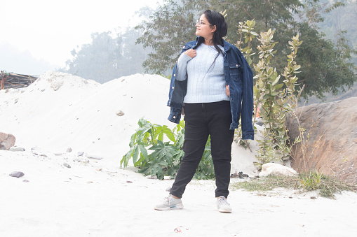 Peaceful scene in Rishikesh, A happy woman, denim jacket on her shoulder, enjoying the calm view from the white sand, Uttarakhand