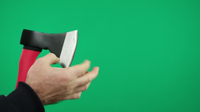Male hands holding an ax on a green background and checking how sharp it is.