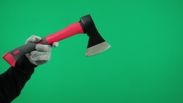 A man's hand holds an ax on a green background wearing gray gloves.