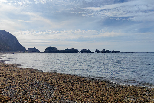 serene beach with rocky formations, calm waters, and a cloudy sky creating a peaceful atmosphere