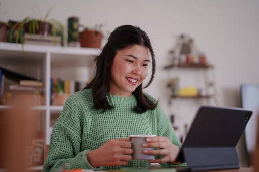 Millennial Asian woman using digital tablet, working at home office