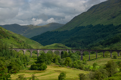 Dramatic mountain scenery of Scottish Highlands with famous Glenfinnan Viaduct. An interesting play of sunlight and shadows on the green mountainside and the valley behind picturesque railway viaduct.
