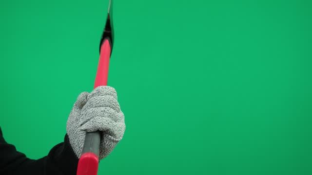 A man's hand holds an ax on a green background wearing gray gloves.