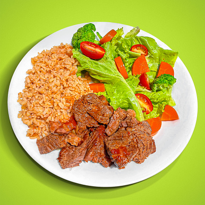 White plate with salad, rice and meat isolated on green background