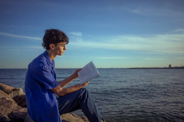 Young kid reading a story while relaxing on a rocky shore