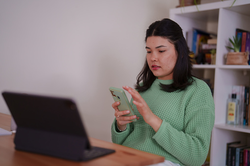 Millennial Asian woman using digital tablet, working at home office