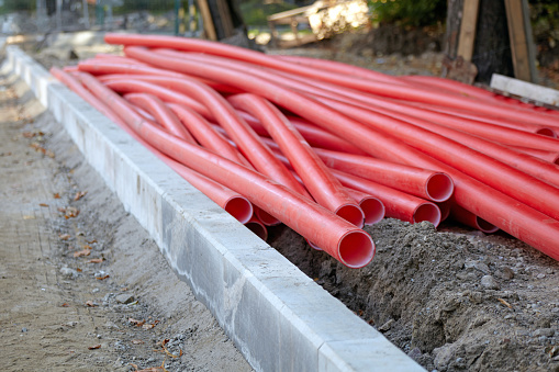 Red plastic utility pipes piled at a road repair site.