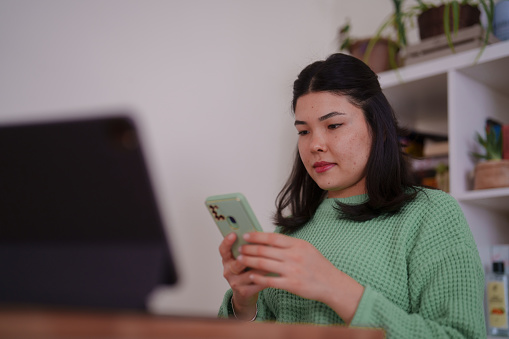 Millennial Asian woman using digital tablet, working at home office