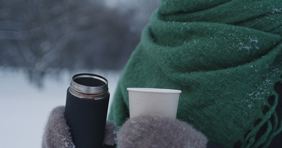 teenage girl pouring hot cocoa into paper cup in park on a winter day, wide photo
