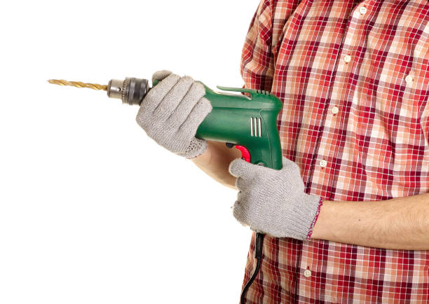 A person is supporting the drill bit he has put in a drill to make a hole right in the sign he has put on the wall.