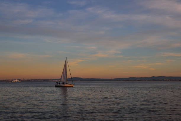 A tiny sailboats cruise on water during sunset