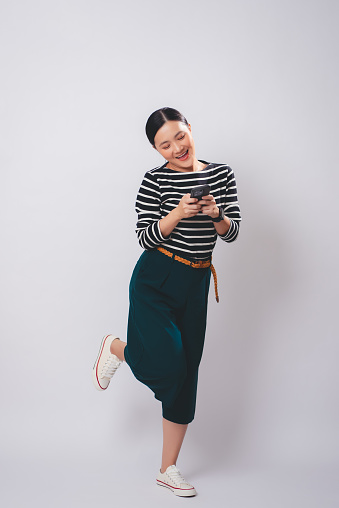 Asian woman enjoying using smartphone standing isolated over white background.