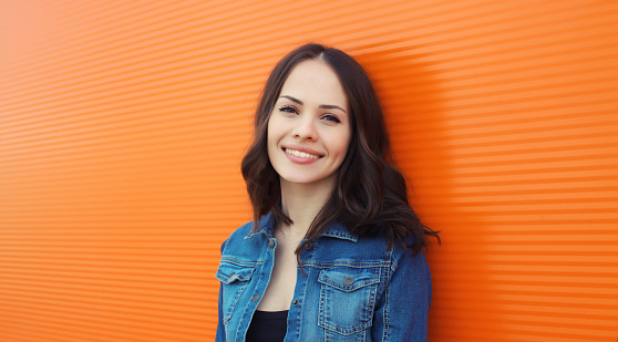 Portrait of happy smiling brunette young woman looking at camera posing on orange background