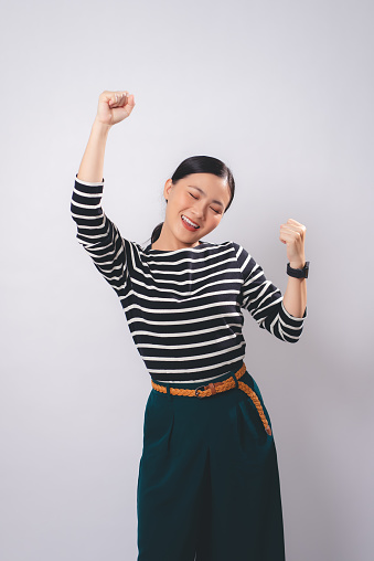 Asian woman happy smiling showing a winning gesture standing isolated on white background.