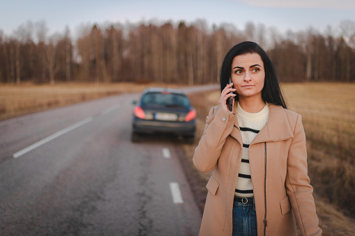 Young woman is stranded on the road because her car broke down. She is phoning for help.