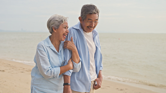 An elderly couple laughs together during a relaxed, joyful moment on a sandy beach, embodying love and companionship in retirement.