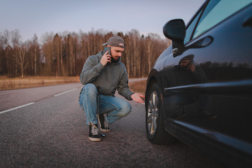 Young man trying to change a flat tire while being stranded on the side of the road.