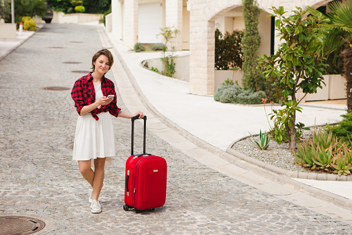 Young woman in a red shirt with a suitcase and phone on the city street