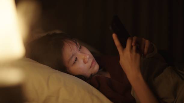 girl using smartphone on bed at night. - teenager problems typing teenagers only ストックフォトと画像