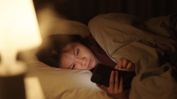 girl using smartphone on bed at night. - teenager problems typing teenagers only ストックフォトと画像