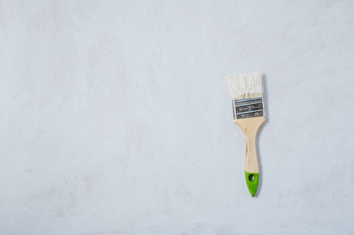 Paintbrush with paint on a white primed floor surface. Preparing the walls and floors of the house for painting. Free space for text