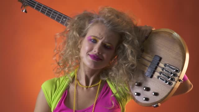Blonde woman in retro clothes, dances and poses with guitar on her shoulder