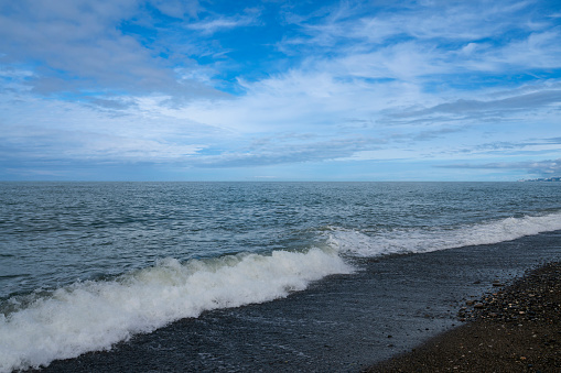 An incoming wave on the Black Sea and a pebble beach on the Sochi coast on a sunny summer day with clouds, Sochi, Krasnodar Territory, Russia