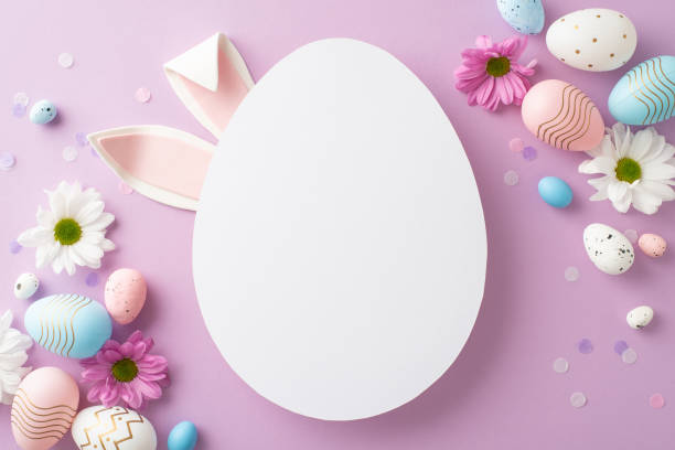 istock Glamorous Easter concept image. Top view of eggs, blooming chrysanthemums, confetti scattered on pastel lilac surface with bunny ears emerging from empty egg-shaped slot for greetings or advertising 2075743430