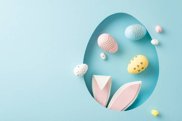 istock Enchanting Easter creativity snapshot: top view of bunny statuette, adorned with pussy willow, and colored eggs, sticking out from an egg-like hollow on tranquil blue field, with niche for your words 2075743439