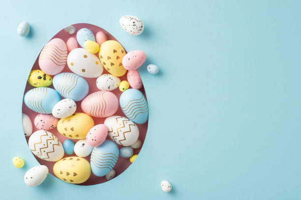 istock Easter celebration concept image. Top view of bright multicolored eggs seen through an egg-shaped opening on a pastel blue backdrop, with space for custom messages or advertising 2075743440