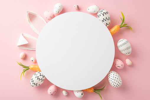 Easter craft inspiration: Top view of simple hued eggs, winsome bunny ears, and carrot offerings for the Easter Hare on a muted pink base, with a round void for inserting text