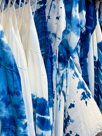 Stock photo showing department store clothes display of customised blue and white tie dyed denim, sundresses on clothes rail in women's clothing section.