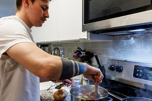 Soldier return to home life: Concentrated Hispanic man with Navy officer tattoo cooking potatoes in domestic kitchen