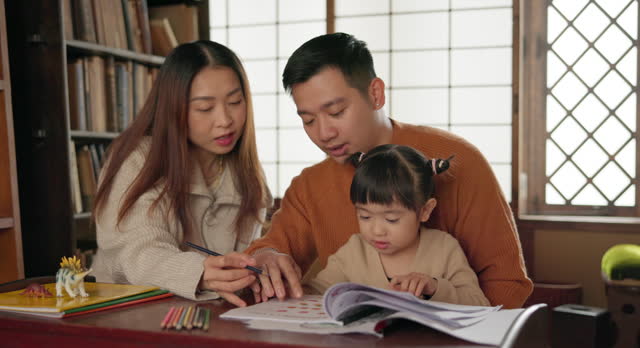Japanese parents, child and education with homework, writing and books for study, development and helping hand. Dad, mother and daughter with notes, pen and check progress in family house with study
