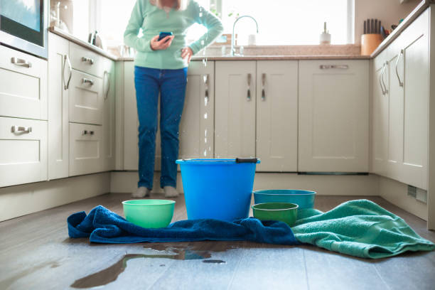 worried home owner dealing with water leak in the kitchen - beschadigd stockfoto's en -beelden
