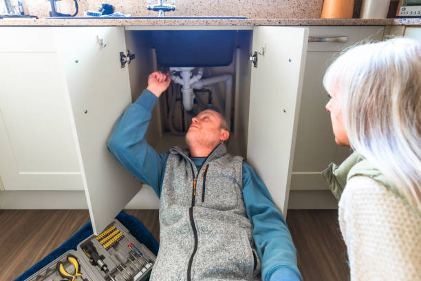 istock Plumber looking at pipes under kitchen sink with home owner observing 2075835410