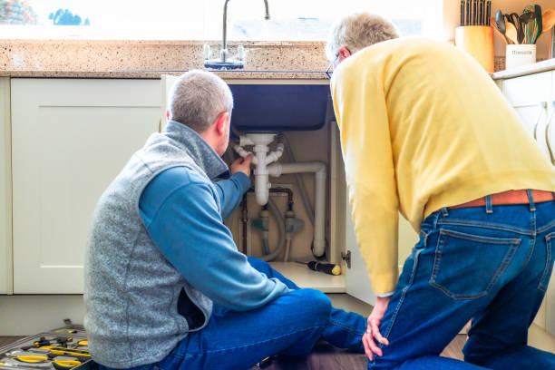 istock Plumber looking at pipes under kitchen sink with home owner observing 2075853227