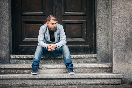 Sad hopeless man sitting in front of an abandoned building