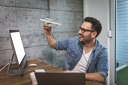 Young handsome successful smiling freelance entrepreneur having fun and showing little model of airplane, explaining how it flies.