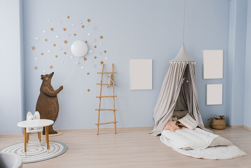 The interior of the children's room is decorated in blue and beige colors. The bear holds a small balloon in his hands. Slide with a pool made of plastic balls. Tent bed with pillows and toys