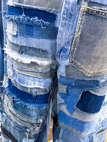 Stock photo showing close-up view of a pair of blue denim jeans sporting a customised design of bleached patchwork, to make them look like expensive designer jeans.