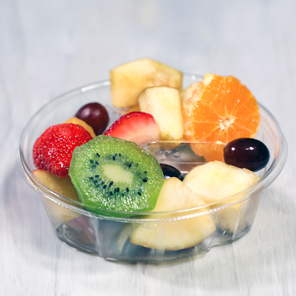 A vibrant assortment of fresh fruits, including strawberries, kiwis, oranges, and grapes, neatly arranged in a clear disposable plastic box, perfect for a healthy snack on the go.