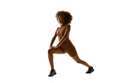 Fitness instructor demonstrating lunge training in brown activewear against white studio white background. Exercises for legs. Concept of sport, mourning routine, active and healthy lifestyle, action.
