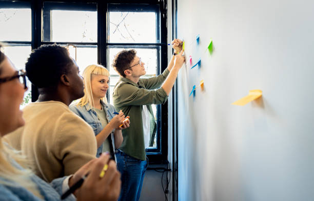 istock Diverse group of young business people working in office using colorful sticky notes on wall to organize their ideas. 2075879022