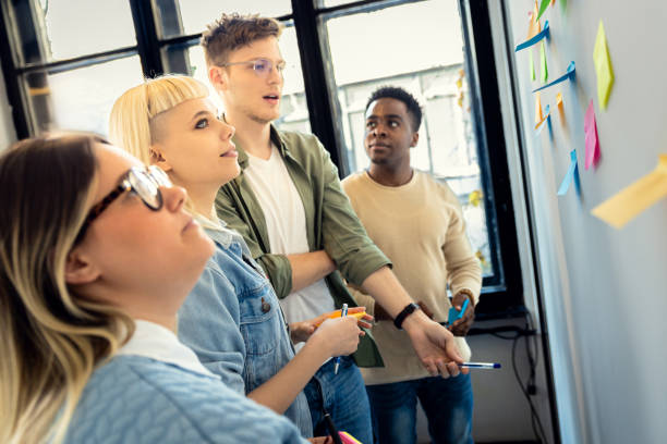 istock Diverse group of young business people working in office using colorful sticky notes on wall to organize their ideas. 2075879023