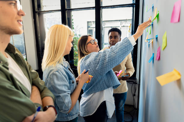 istock Diverse group of young business people working in office using colorful sticky notes on wall to organize their ideas. 2075879025