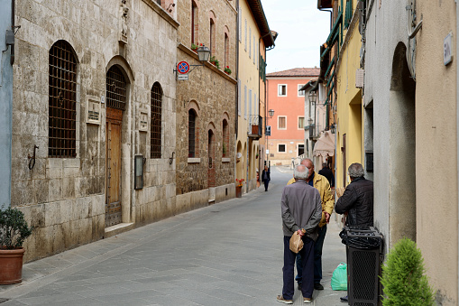 San Quirico d'Orcia, Province of Siena, Tuscany, Italy - 25 October 2022: Italian men have bought food and are talking on the street of San Quirico d'Orcia. The city is a comune of about 2,500 inhabitants in the Province of Siena in the Italian region Tuscany, located about 80 kilometres southeast of Florence and about 35 kilometres southeast of Siena inside the Valdorcia landscape. It is named in honor of Saint Quiricus.