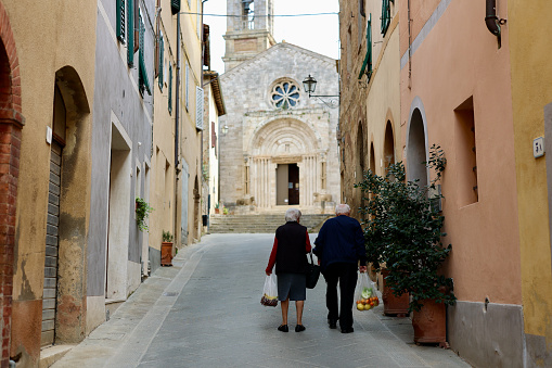 San Quirico d'Orcia, Province of Siena, Tuscany, Italy - 25 October 2022: A couple of Italian elderly people return home after the grocery market. San Quirico d'Orcia is a comune of about 2,500 inhabitants in the Province of Siena in the Italian region Tuscany, located about 80 kilometres southeast of Florence and about 35 kilometres southeast of Siena inside the Valdorcia landscape. It is named in honor of Saint Quiricus.